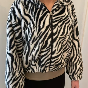 Luvjacka zebra - Luvjacka med mjukt "gossedjurstyg". Zebramönstrad. Boxig fit. Personen på bilden har storlek XS-S. Fodrad med vitt tyg.