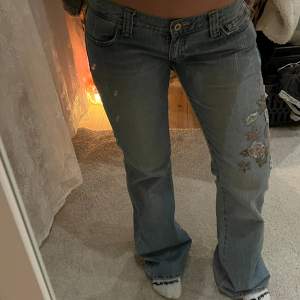 Vintage jeans med unika blommdetaljer. I en ljus tvätt och lågmidjade.  Mått:  Midja: 42 cm  Ytterbenslängd: 102 cm Innerbenslängd: 84 cm  Gren: 18 cm 