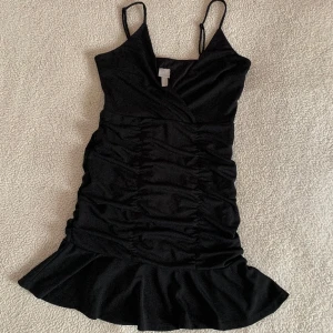 H&M trend svart volangklänning med scrunch - Otroligt snygg klänning från H&M trend med scrunch på sidor och i rumpan/ryggen. Aldrig använd. I nyskick utan anmärkningar.