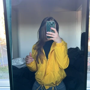 Gul vindjacka - Väldigt snygg jacka ifrån H&M. Går att stylea snyggt för den som är bekväm i utstickande färger. Går att dra in i midjan om man vill. Väldigt bra skick. Stl XS.