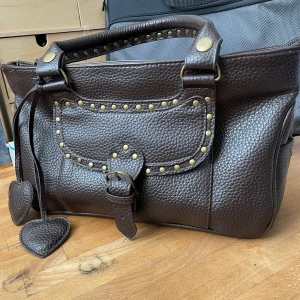 Handväska - Väska med söta detaljer, två fack invändigt. Spännen till att koppla på axelräm finns invändigt. Använd sparsamt, inga skador