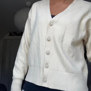 Kofta med detaljer - Säljer denna jätte fina beiga koftan med pärljdetaljer på knapparna. Använd en gång och är i nyskick. Nypris ca 500kr.
