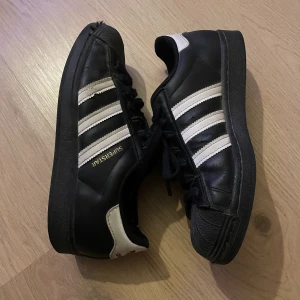 Adidas superstars svarta - Säljer dessa skor då de inte kommit till användning. Endast använda fåtal gånger men lite defekter. Jag vet inte vad det är för storlek eftersom det är i engelsk storlek men jag tror det är 40