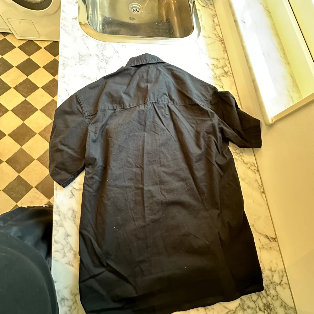 En svart kortärmad HM skjorta med storlek XS i passformen relaxed fit. En tunn skjorta som är perfekt i sommarvädret. Använts endast 2-3 gånger så funkar precis som ny. . Skjortor.