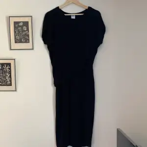 En svart klänning med korta ärmar och ”omlott” vid magen. Sitter jättefint och i bra skick!