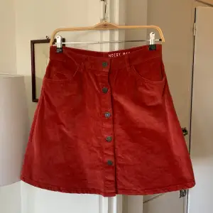 En kort röd/orange kjol i manchester-tyg. Aldrig använd och i jättebra skick!