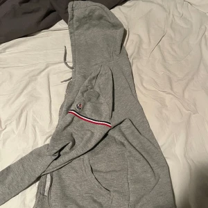 Moncler tjocktröja  - Säljer för att den har blivit för liten. Finns ett problem och de är att man inte kan knäppa hoodien för att dragkedjan man håller i när man knäpper har ramlat av, finns säkert att köpa en dragkedja som man håller så att den går att stänga. Skick 9/10
