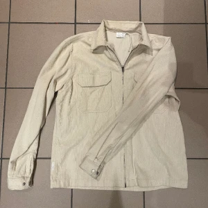 YOKE OVERSHIRT - En beige overshirt i Manchester material jag köpte för 3 år sedan på junkyard vid Drottninggatan för 1100kr. Den är knappast använd. 9.5/10 skick. Hör av dig vid frågor och funderingar!  PRISET ÄR PRUTBART!!!