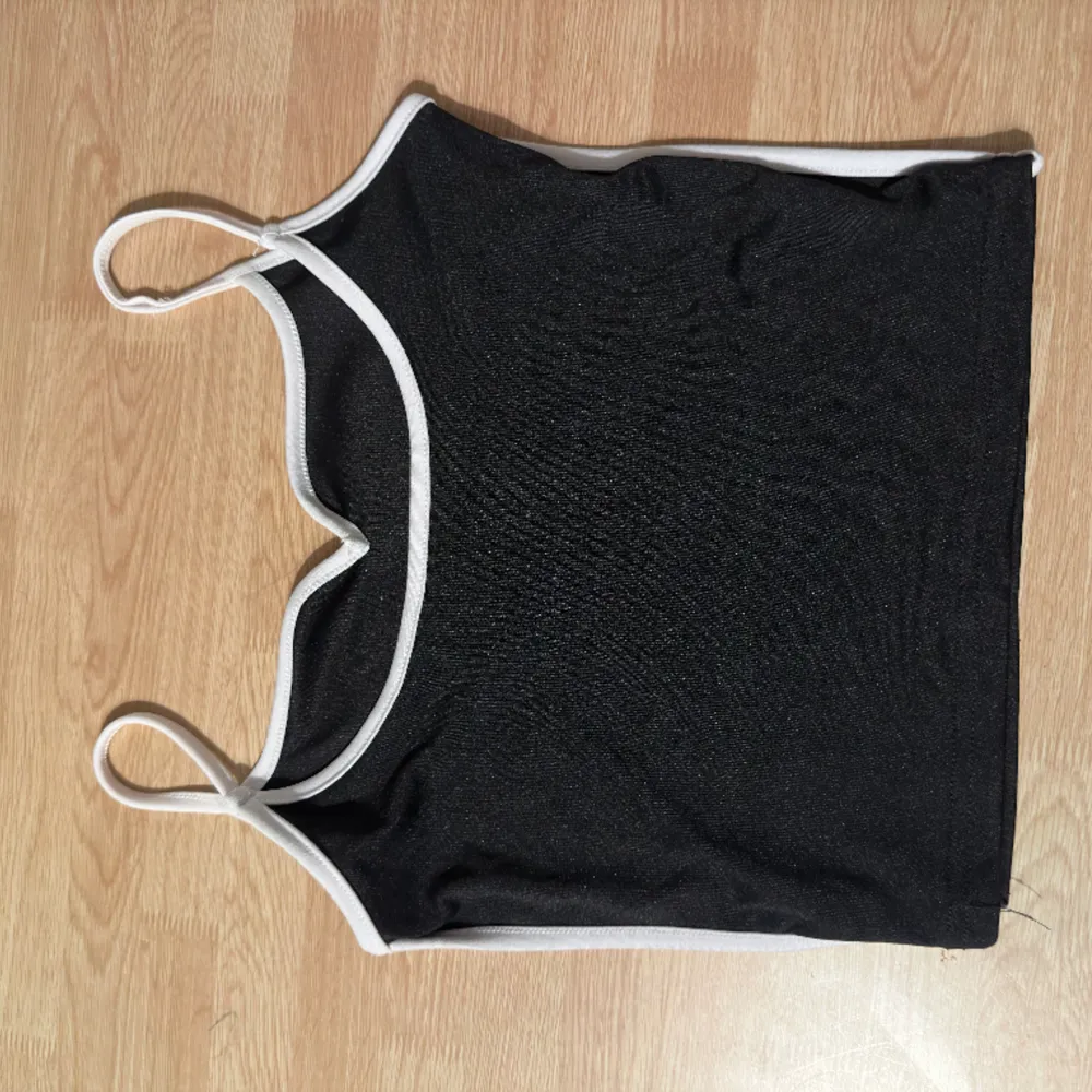 Snygg svart topp med band och vita detaljer runt formen på tröjan. Oanvänd, testad endast.. Toppar.