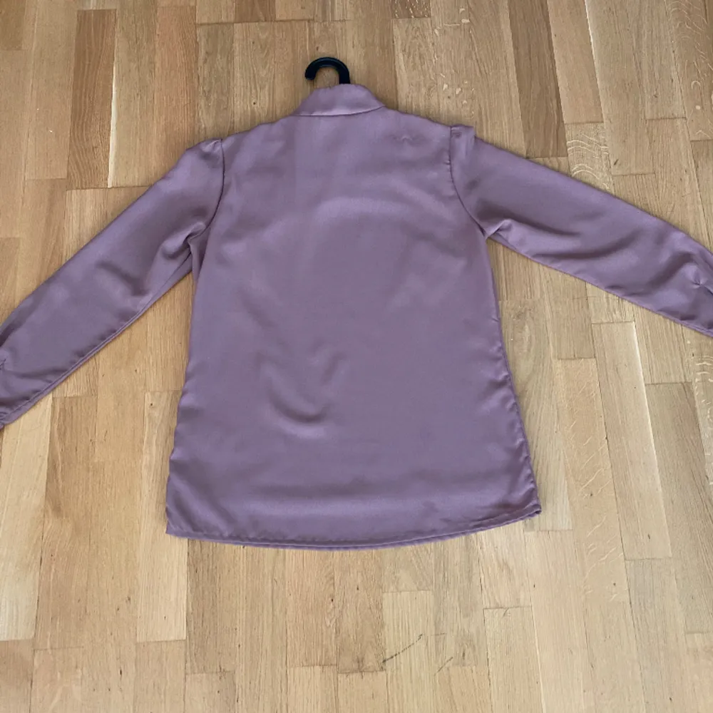 En elegant fuchsiarosa blus från Bonprix /Bodyflirt i storlek 40. Blusen har vackra volanger runt halsringning. Den är långärmad. Blusen har flera knappar i nacken framme. Längd: 73 cm. Blusen användes ett par gånger och är i bra skick.. Puserot.
