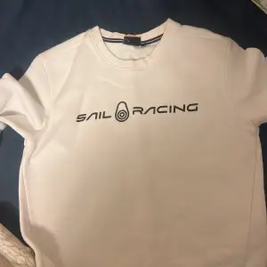 Den är vit med svarta bokstäver på Sail racing tröja som är exakt ny