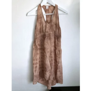 Beige batik klänning, 36/38 S, tunika, tie-dye, bohemisk, boho, brun, chiffong - Batikad klänning i chiffong, rynkad detalj fram med elastiskt band, längre bak. Finns hål i nederkant vid fållen. Mått i cm: bröstvidd 44; längd fram från axeln 86.