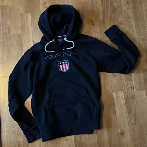 Gant hoodie  - Gant hoodie, mörkt grå nästan svart, fint använt skick, storlek M. Prisförslag. Frakt tillkommer 
