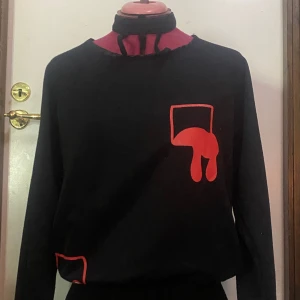 Tjocktröjan med design på  - Köpt på Närcon för några år sendan men nästan aldrig andvänd. Har resår på en stor del längst ner och en chocker som man inte kan ta av från tröjan. Är i bra skick kan vara lite stora vid axlarna och vet inte storlek men skulle gissa M-L