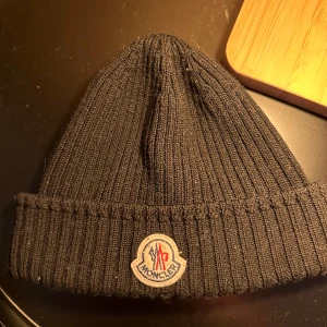 Moncler mössa  - Säljer min Moncler mössa då den inte kommer till användning, inköpt på NK för 2 år sedan! Taggen inuti sitter lite löst, bortsätt från det inga tecken på slitage 