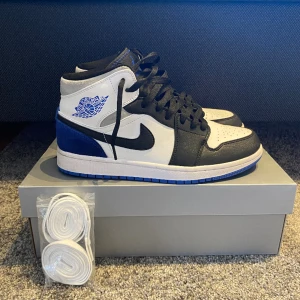 Air Jordan 1 Mid SE "Game Royal Black Toe" sneakers - Väldigt fräscha, använda ett par fåtal gånger. Kan ta mer bilder om så önskas. Ej originalbox men boxen på bilden medkommer och ett par extra vita skosnören. Frakt ingår. 