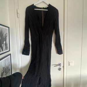 Så fin svart klänning med djup urringning och långa ärmar. Finns dragkedja på ryggen och slits. 