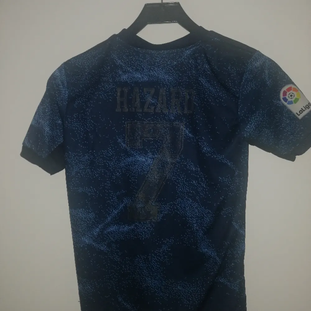 Säljer ett real Madrid set med tröja och shorts. Skicket är okej men använt. Nummer 7 på ryggen med Hazard. Storlek 164 så ungefär xs. T-shirts.