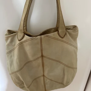 Beige tote väska läder - En beige väska köpt second hand. Bra skick, tillräckligt stor för att ha t.ex dator i. Perfekt till skola/jobb! Skriv gärna vid frågor/bud!