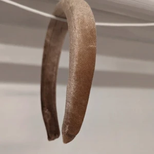 Beige diadem - Ett elegant beige diadem med en mjuk och glansig yta från Søstrene Grene,Perfekt för att komplettera en stilren look.fint skick lite trådlösa men Inget som stör (vg och se bilder) 