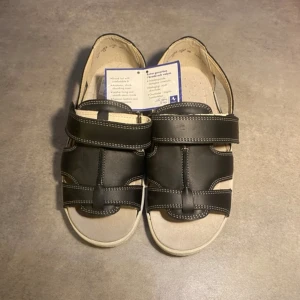 Sandaler- svart/beige - Klavanss hästen sandaler med bred läst i mycket bra kvalitet. Skorna är nya med prislapp. Det står att skorna är st 36 men passar även någon som är 38.