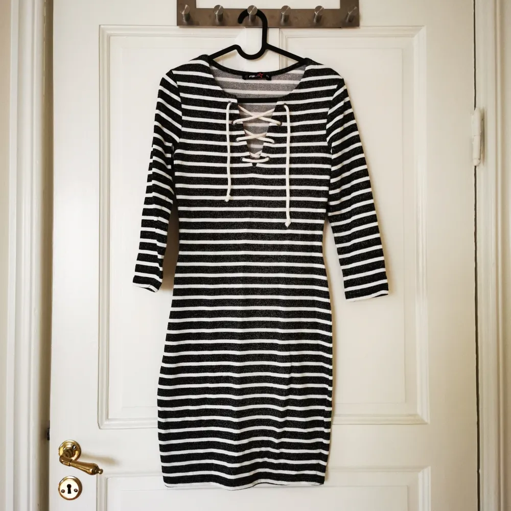 En svart och vit randig klänning från FB Sister med trekvartsärmar och snörning framtill. Klänningen har en tight passform och är tillverkad i ett bekvämt material.. Klänningar.