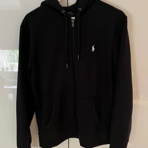 Ralph Lauren Zip Hoodie Svart - En svart helt oanvänd Ralph Lauren Zip Hoodie. Säljes pga för stor. Den är i storlek M. Nypris 2200kr säljes för 1100kr. 
