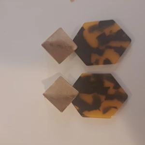 Örhängen med hexagonform - Ett par örhängen med en unik design. Örhängena består av två delar: en mindre fyrkantig del i guld och en större hexagonformad del med ett mönster i brunt och gult.