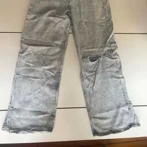 Stentvättademede ljust gråblå jeans med vida ben och ett par revor/hål (inte slitage utan nött look). Skrynkliga på bilden. 