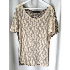 Oversize t-shirt, spets, leopard, gräddvit, naturvit, Jeane Blush - Oversize t-shirt från Jeane Blush i storlek XS (men passar definitivt fler, se mått). Framsidan är av gräddvit spets, baksidan av leopardmönstrad mjuk tunn velour. Vid halsringning, stretchig. Mått i cm: bröstvidd 56; längd fram från axeln 75.