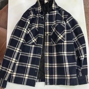 Marinblå rutig vårjacka/overshirt - Marinblå rutig overshirt/jacka från H&M. Passar riktigt bra för vårvädret, säljs då den inte används. Storlek S men riktigt stor så den passar som M.