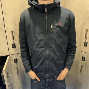 Polo Ralph Lauren Jacka - En perfekt jacka nu till våren som inte är för kall eller för varm. Jackan har tvättats sen senaste användning och impregneringen kan ha gått bort så det kan behövas göra innan använding i regn. Annars är det mindre skador som är onsynliga.🗿👍