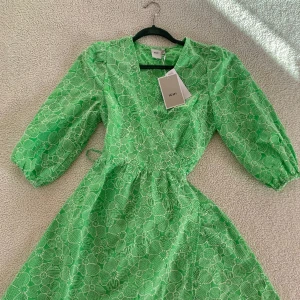 ICHI grön sommarklänning med omlott och brodyr - Otroligt vacker omlottklänning från ICHI i grön livlig färg med vita broderade blommor. Ny med tags kvar. Storlek XS men passar definitivt även en S då den upplevs rymlig. Knyts på sidan med snöre. Kan skicka fler bilder vid intresse 🌹 Nypris 899kr.