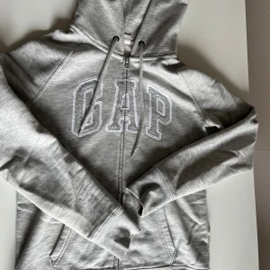 Gap hoodie - Ljusgrå gap hoodie som är köpt på Sellpy. Den har ett litet hål vid sömmen på sidan (bild 3) som var där när jag köpte den men som lätt kan sys igen! Bra skick annars💕