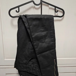 Svarta byxor från NLY Trend - Svarta byxor från NLY Trend i storlek 36. Byxorna har en quiltad detalj på knäna och flera fickor fram och bak. De är tillverkade i ett syntetmaterial och har en knapp och dragkedja framtill.