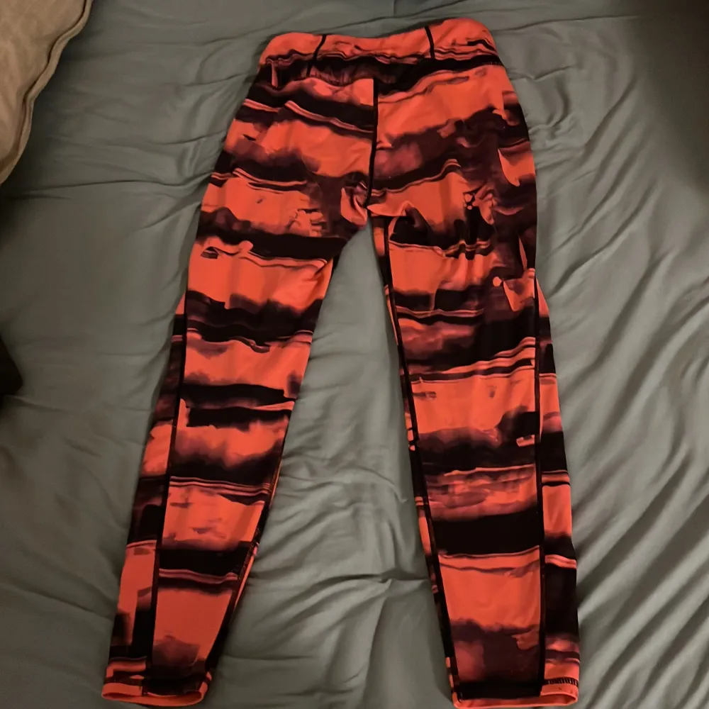 Ett par orange och svarta leggings från H&M Sport. Byxorna har ett abstrakt mönster och är tillverkade i ett stretchigt material som passar bra för träning.. Sportswear.