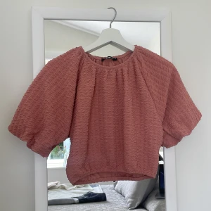 Fin rosa blus i skrynkligt material - En kort rosa blus med ärmar till armbågarna med ett skrynkligt tyg