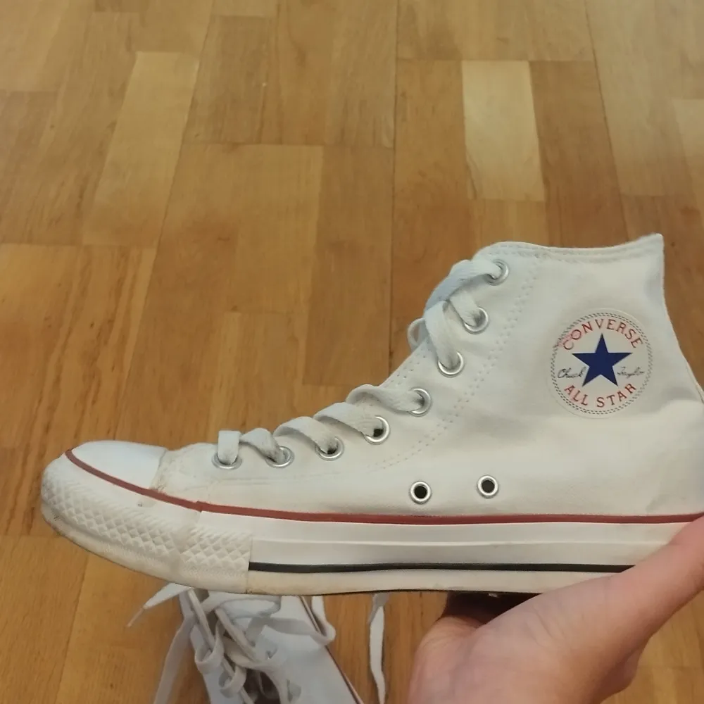 Ett par vita sneakers från Converse med snörning och den klassiska Converse All Star-logotypen på sidan. Skorna har en vit sula med en röd rand. Den är sparsam använd. Pris kan sänkas vid snabb affär.. Skor.