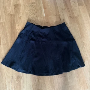 Svart kortkjol - En svart kortkjol i ett enkelt och stilrent utförande. Kjolen har en lätt utställd form och är tillverkad i ett mjukt material.