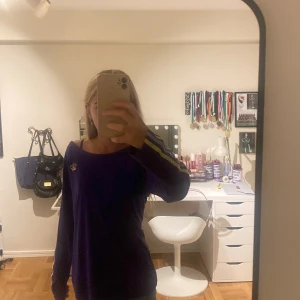 Långärmad lila of shoulder tröja med öppen rygg 💜 - Lila långärmad of shoulder tröja med lite öppen rygg. Ett samarbete mellan Victoria Beckham och Addidas (info från den ba köpte den ifrån). Se märket på bild 3. Ganska bra skick utom märker/symbolen som inte sitter så bra se bild 3 igen. Fråga på💗!