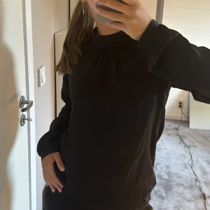 Blus i satin  - Säljer en svart blus i satin med struktur på övre ryggen med två knappar bak. 