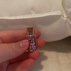 Rosa glitter i glasflaska - En liten glasflaska med kork innehållande rosa glitter. Perfekt för att lägga till en glittrande effekt på smink eller naglar.