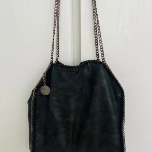 Stella Maccartney väska  - Säljer en svart & glittrig väska från Stella Maccartney   Lite sliten på ena sidan och lite av färgen på kedjan har gått av men den har fortfarande mer att ge😊