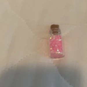 Halsband med rosa kristaller i glasflaska - Ett halsband med en liten glasflaska fylld med rosa kristaller och en kork som lock.