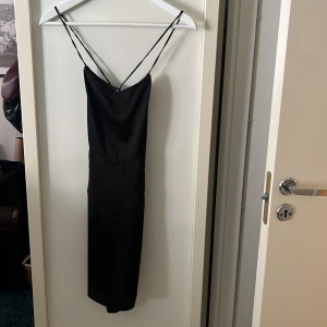 Svart kort klänning  - Svart kort klänning med öppen rygg och korsade straps. Tunt material. Från Asos. Storlek 36.