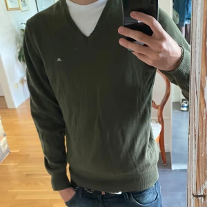 Grön J.Lindeberg Tröja. - J.Lindeberg tröj i hyfsat skick, storlek M men passar även S. Defekter finns en liten fläck på framsidan av tröjan men syns knappt, kan kankse gå bort i tvätt. Finns även några små hål som man ser längst ner på andra bilden.  Pris 199kr kan diskutera