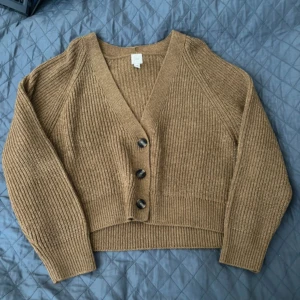 Brun stickad kofta från H&M - En oanvänd brun stickad kofta från H&M med långa ärmar och knappar framtill. Koftan har en ribbad struktur och en v-ringad halsringning.💕