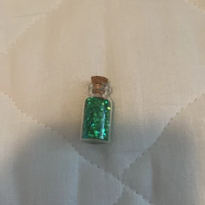 Litet glasflaska med grönt glitter - En liten glasflaska fylld med grönt glitter och försluten med en kork. Perfekt för pyssel eller som dekoration.