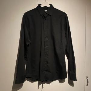 The Shirt Factory Slim Fit Svart Skjorta  - Hej, säljer en fräsch skjorta från The Shirt Factory. Helsvart, slim fit passform. Utmärkt skick, endast använd en gång. Nypris 1200kr. Storlek 39 vilket motsvarar medium. Riktigt snygg passform. Pris kan diskuteras. Hör av dig vid frågor.