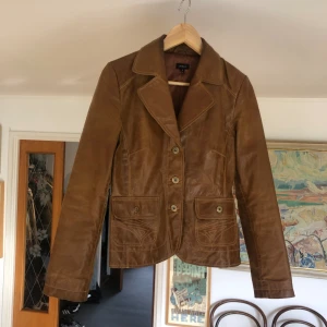 Brun läderjacka - Supersöt läderjacka med coola stygn på fickorna. Perfekt både på våren och kalla sommardagar! Normal i passformen. Säljer eftersom jag inte änvänder den längre (: nypris: 350kr